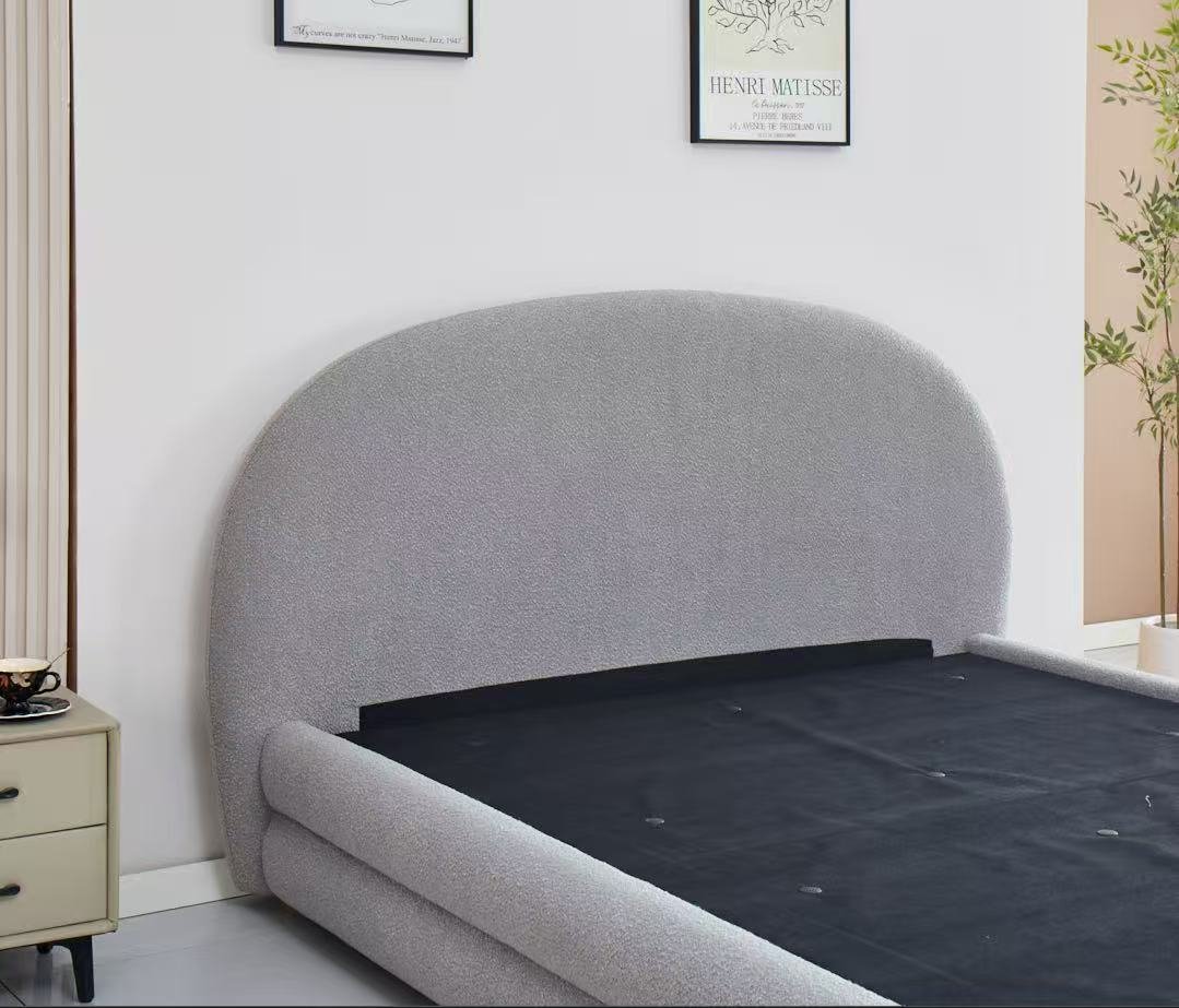 Gray upholstered bed in a room with a white wall and framed pictures.